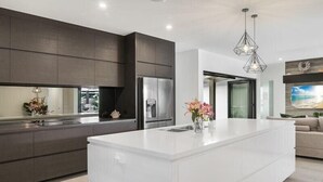 A modern kitchen with a large island, dark cabinetry, stainless steel appliances, and a pendant light. - 4 Bedroom Luxury House in Port Douglas (Port Douglas)
