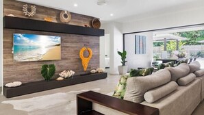 A modern living room with a large flat-screen TV, decorative wall art, and a comfortable sofa. - 4 Bedroom Luxury House in Port Douglas (Port Douglas)