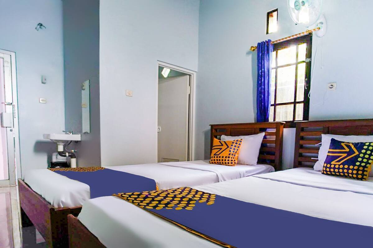 A hotel room with two beds, a sink, and a window with curtains.