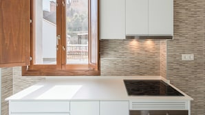 Una cocina moderna con un ventanal grande, armarios blancos y vistas a un castillo.