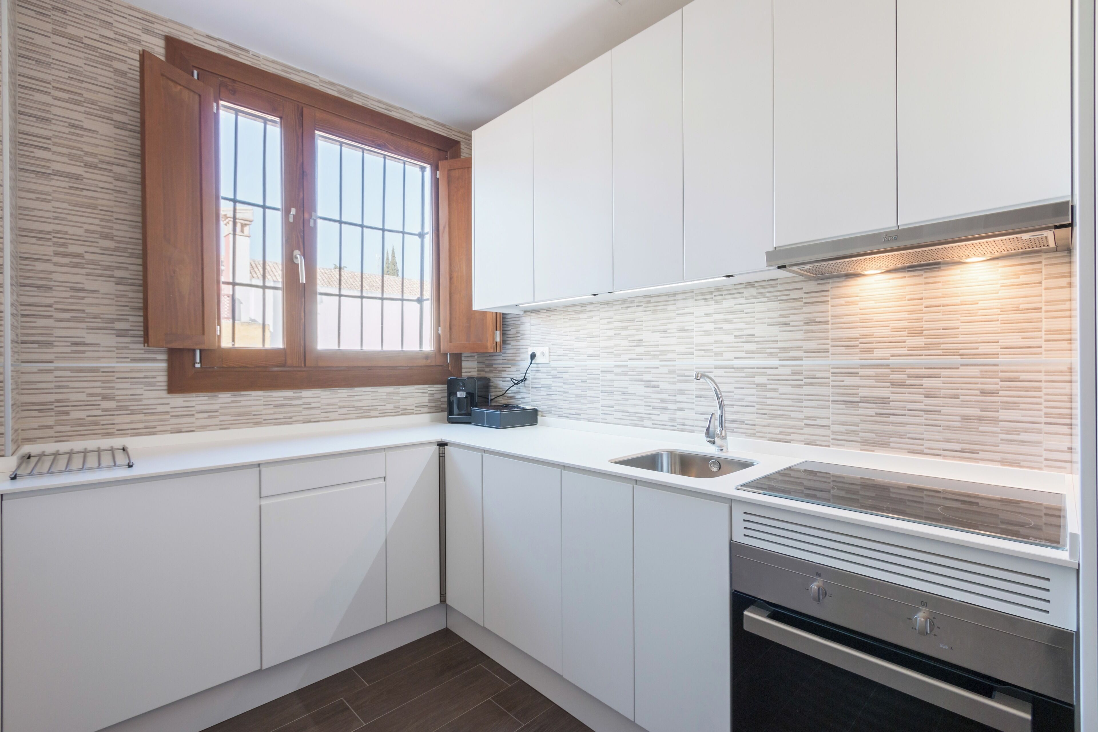 Een moderne keuken met witte kasten, een ingebouwde kookplaat en een raam met houten luiken.