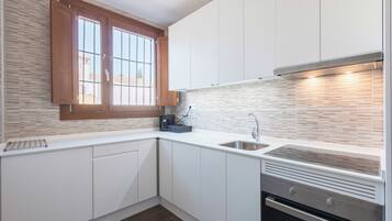 Een moderne keuken met witte kasten, een ingebouwde kookplaat en een raam met houten luiken.