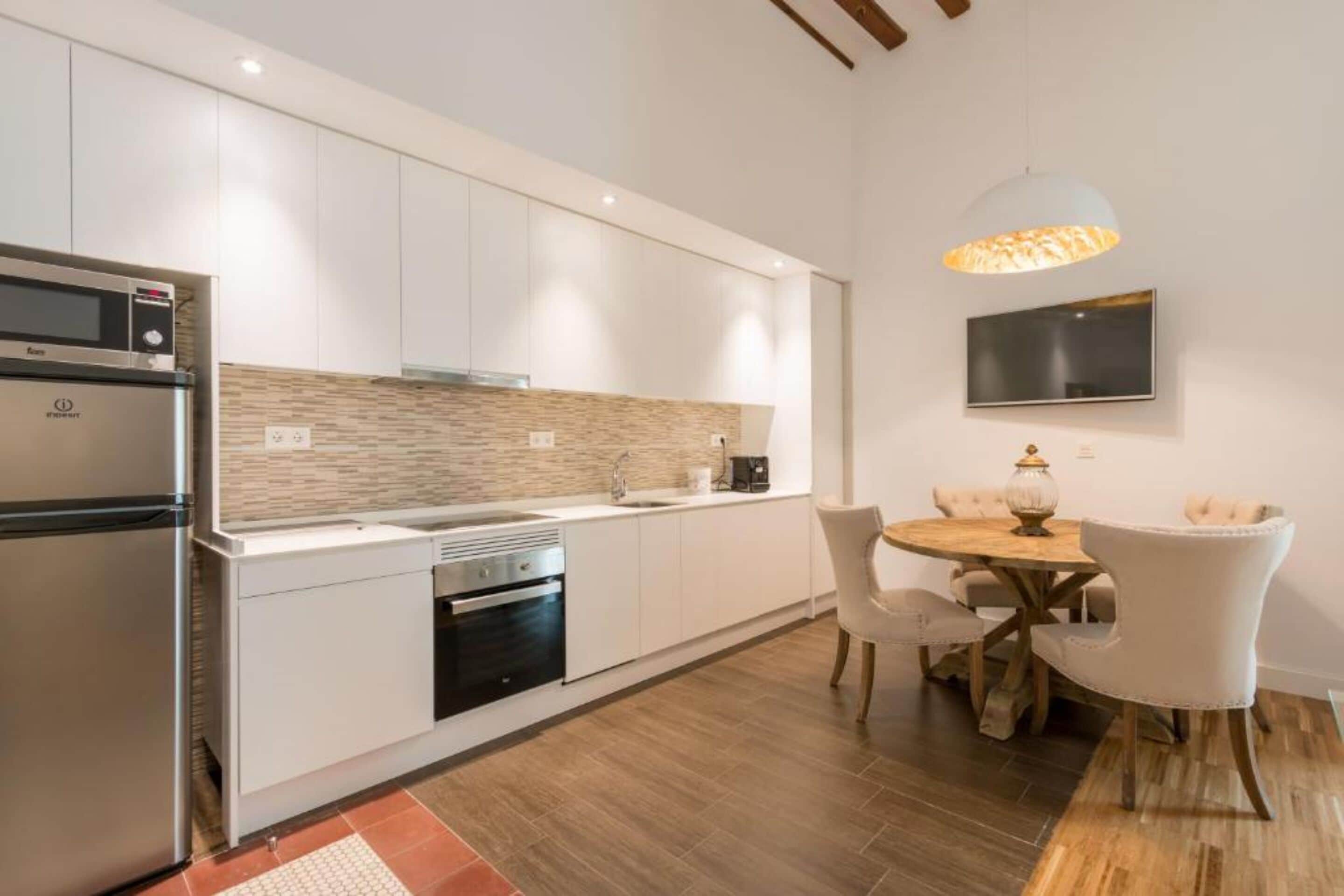 A modern kitchen with white cabinets, a built-in oven, and a dining area with a round table and chairs.