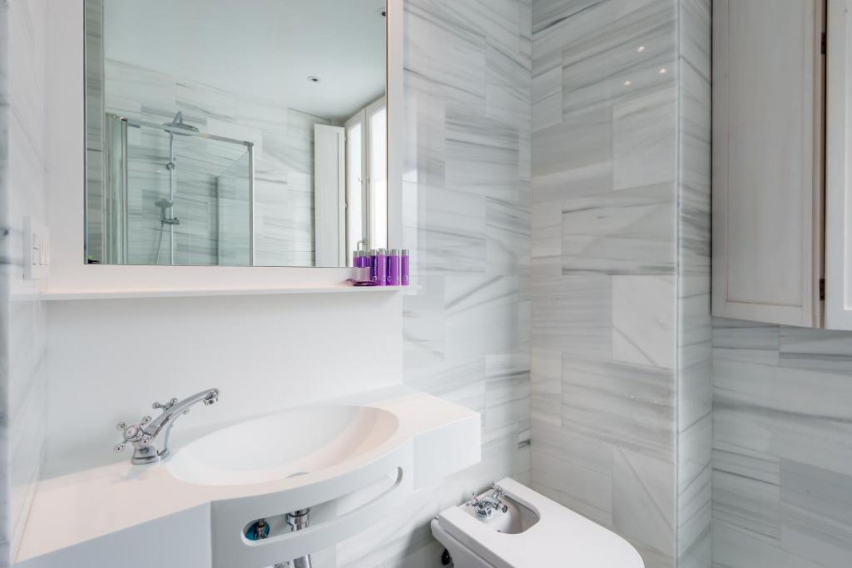 Un baño moderno con lavamanos, tocador y zona de ducha blanca.