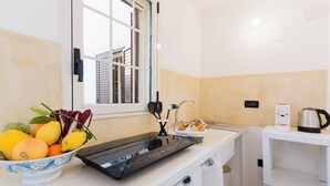 Une cuisine avec un plan de travail, un saladier rempli de fruits, une bouilloire et une fenêtre.