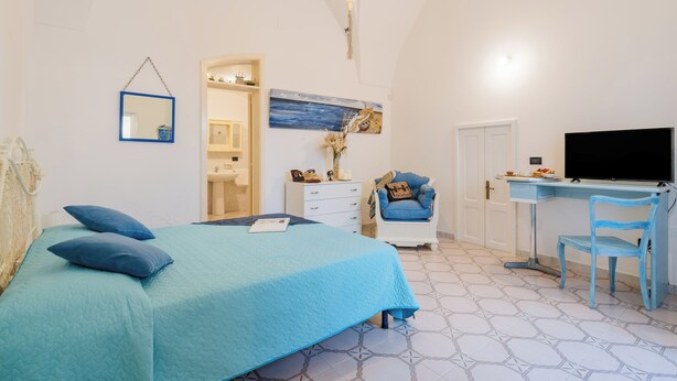 Une chambre à coucher comprenant un lit, un bureau, une chaise, un téléviseur et une salle de bain visible à travers une porte ouverte.