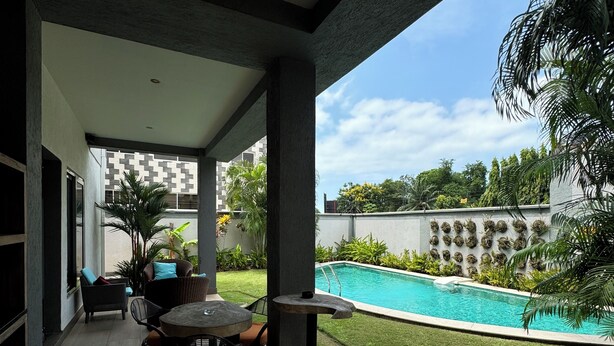 A covered outdoor patio with a pool, seating area, and a decorative wall with planters. - The Palms by Eagles Airport Residential (Accra)