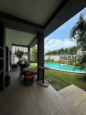 A covered outdoor patio with a pool, seating area, and a decorative wall with planters. - The Palms by Eagles Airport Residential (Accra)