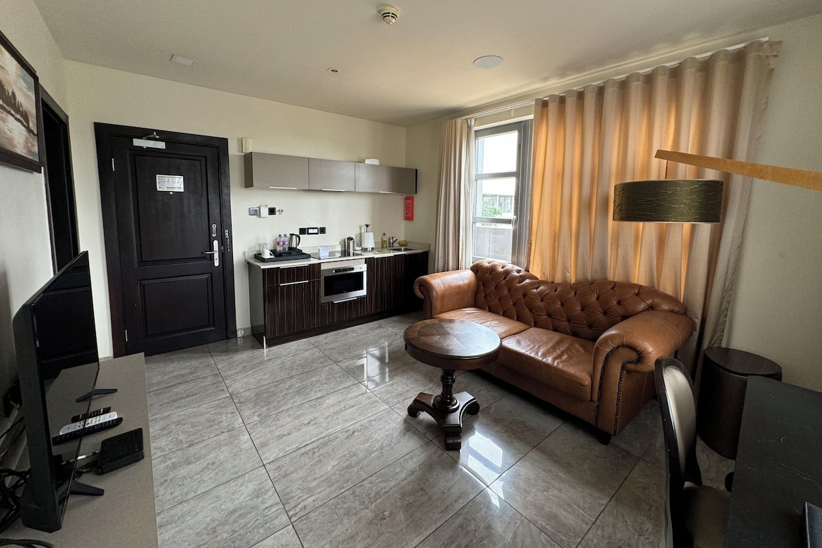 A modern living room with a leather sofa, a small round table, and a kitchen area with a stove and cabinets.