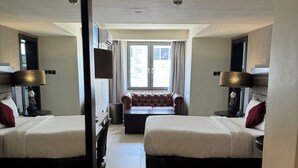 A hotel room with two beds, a sofa, a desk, and a large window. - The Palms by Eagles Airport Residential (Accra)