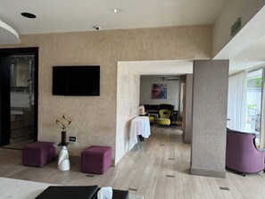 Eine moderne Hotellobby mit einem Flachbildfernseher, einem Essbereich mit gelben Stühlen und einer Treppe mit einer Zierrelung.