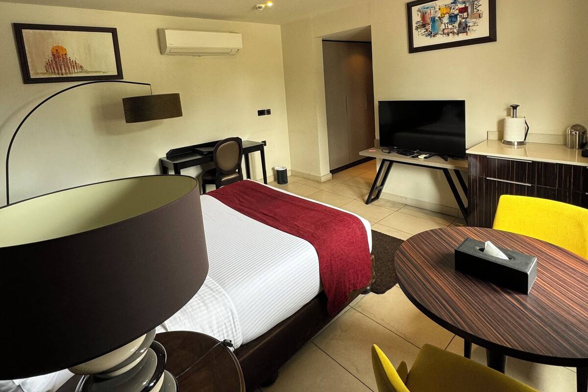 A hotel room with a bed, a desk, a chair, a TV, and a small table with a tissue box.