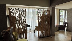 A spacious room with a wooden floor, a seating area with chairs, and a large window with sheer curtains. - The Palms by Eagles Airport Residential (Accra)