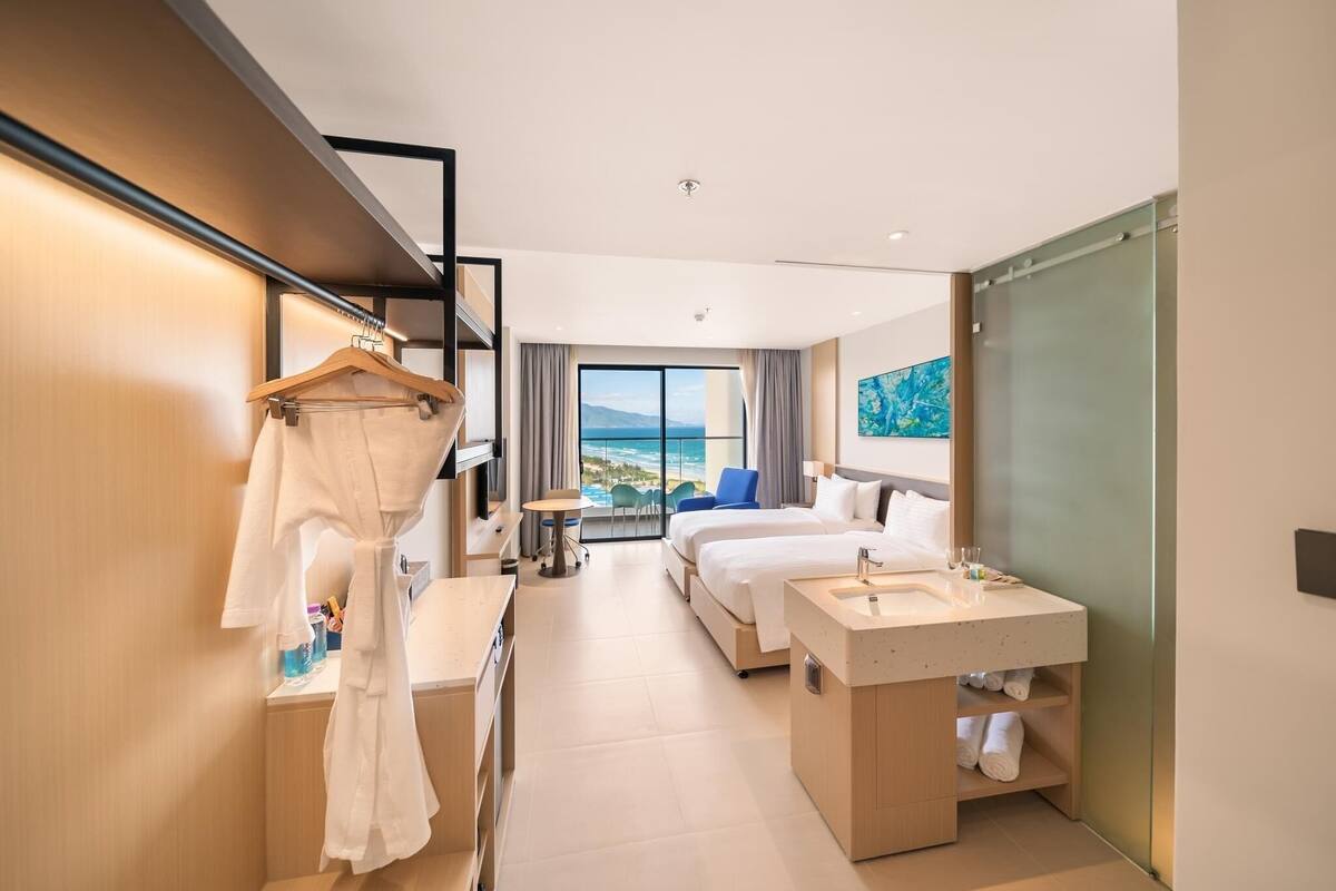 A modern hotel room with a balcony, a bed, a desk, and a bathroom.