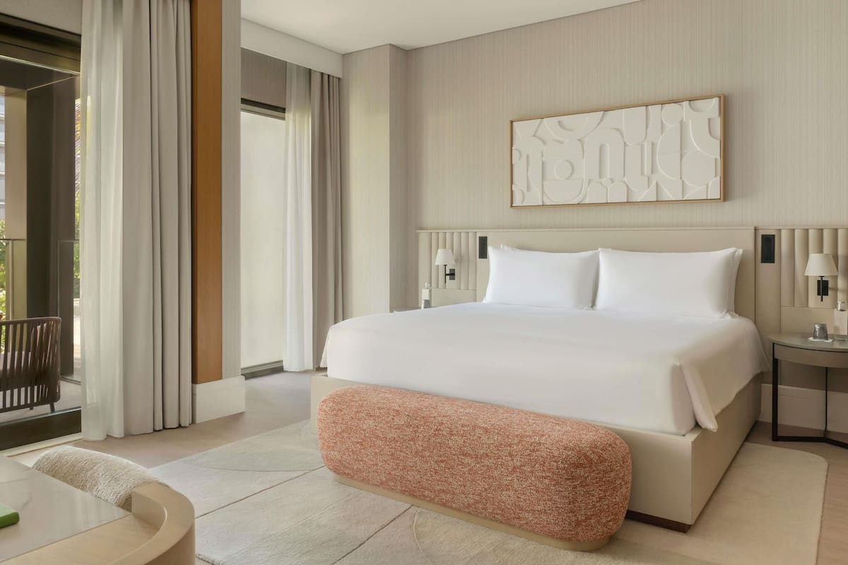 A modern hotel room with a large bed, a small seating area, and a view of the outdoors.