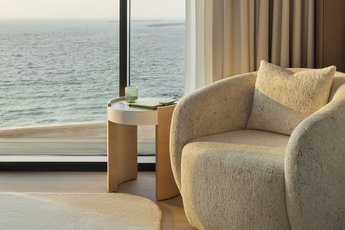 A modern room with a large window, a round beige armchair, and a small wooden side table.