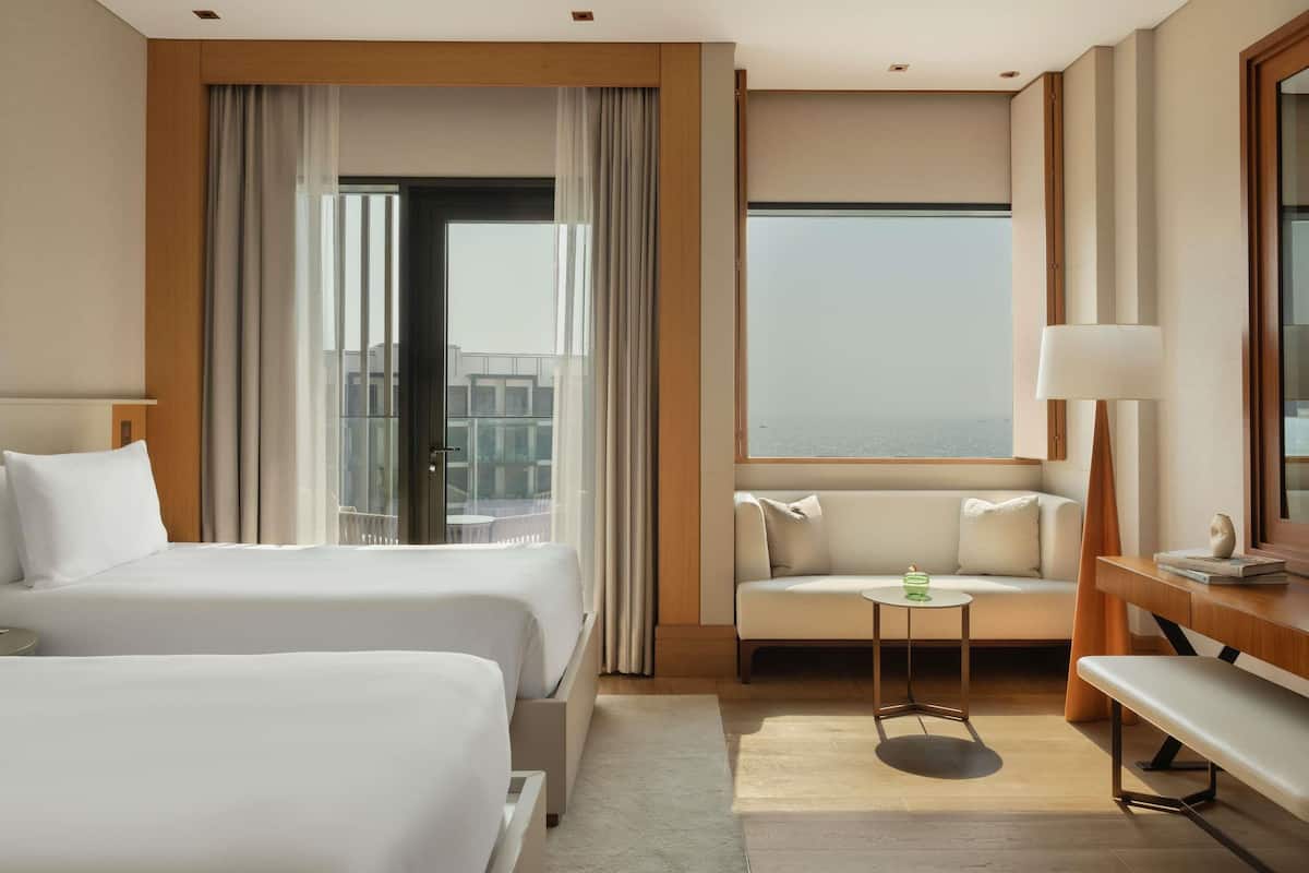 A hotel room with two beds, a sofa, a small table, and a large window with a view.