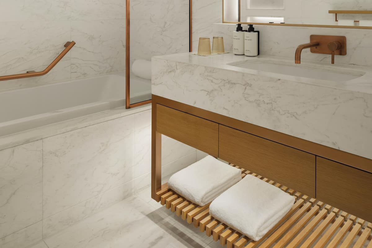 A modern bathroom with a wooden vanity, a large mirror, and a bathtub.