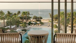 A balcony with a view of a pool and beach, surrounded by palm trees and lounge chairs. - Delano Dubai (Dubai)