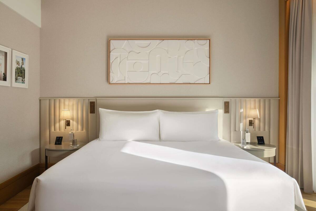 A large bed with a headboard, two bedside tables with lamps, and a wall-mounted artwork.