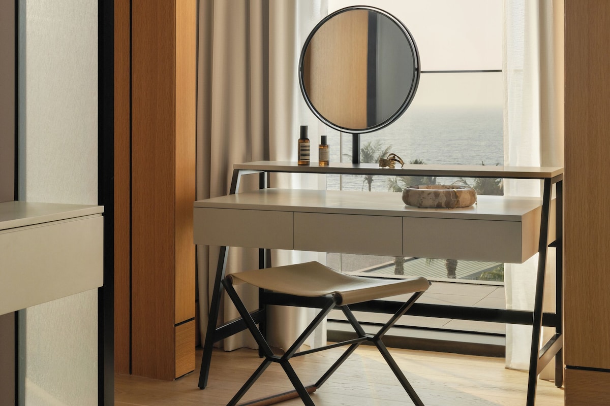 A modern bathroom with a vanity, mirror, and a view of the sea through a large window.