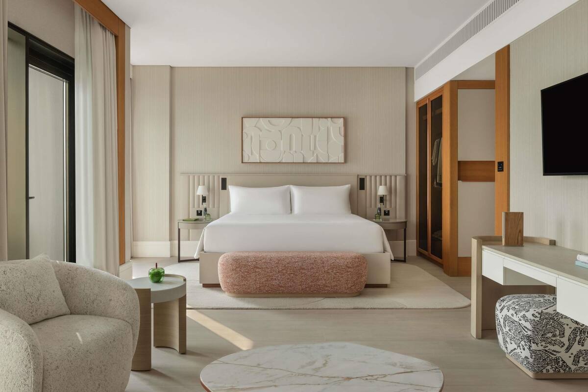 A modern hotel room with a large bed, bedside tables, a desk, a chair, and a television.