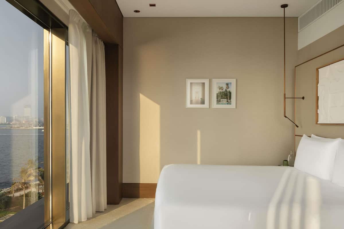 A hotel room with a large window, a bed, and two framed pictures on the wall.