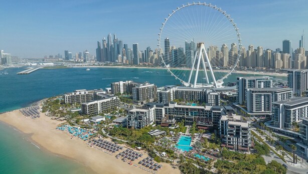 A coastal cityscape with a prominent Ferris wheel, modern high-rise buildings, and a beachfront with sun loungers and a swimming pool. - Delano Dubai (Dubai)