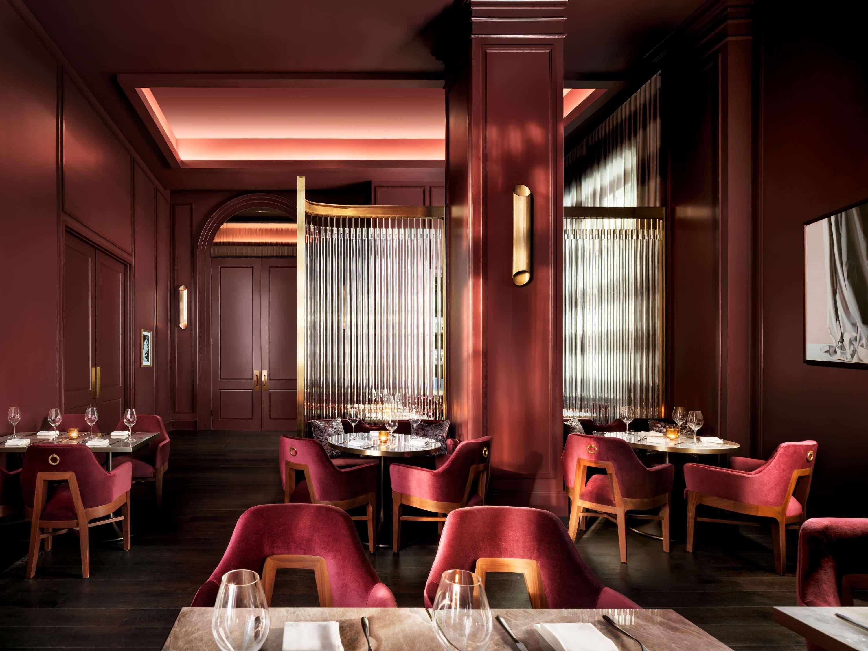 A restaurant with red velvet chairs, a central column, and a dining area with tables set for two.