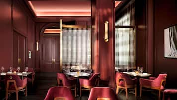 A restaurant with red velvet chairs, a central column, and a dining area with tables set for two.