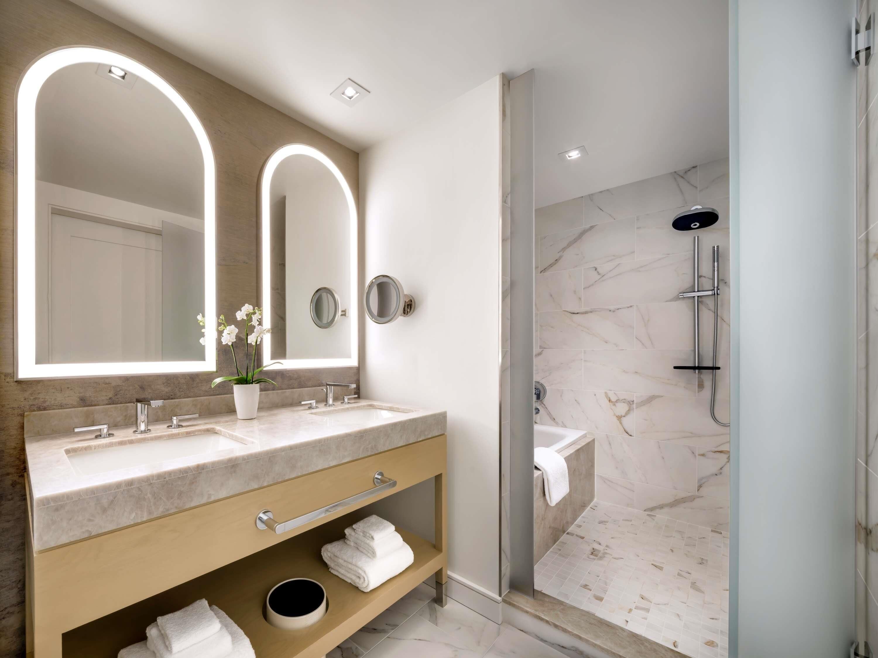 A modern bathroom with a large vanity, two mirrors, a shower with a glass door, and marble flooring.