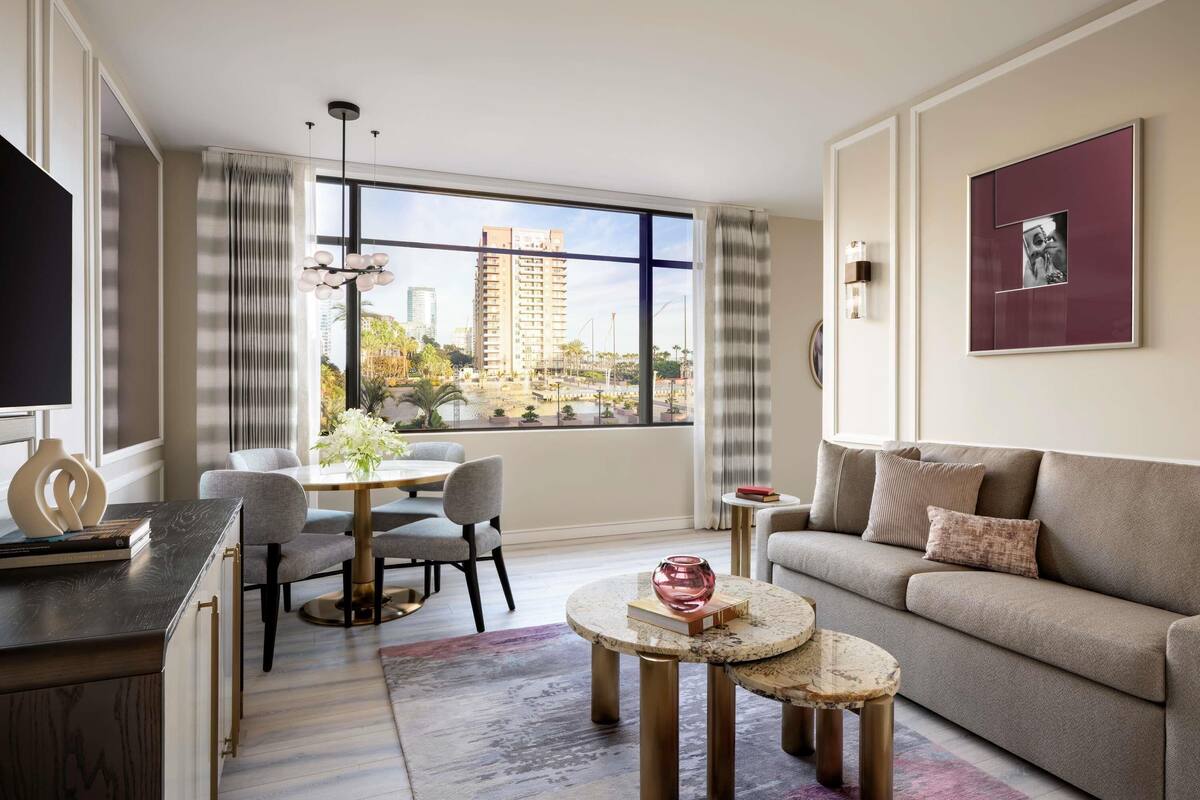 Een moderne woonkamer met een bank, een eettafel met stoelen, een salontafel en een uitzicht op de stad door grote ramen.