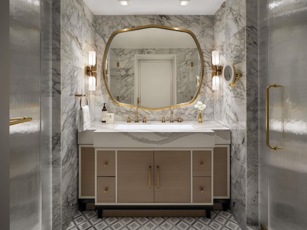 A bathroom with a marble wall, a gold-framed mirror, a white sink, and a wooden vanity with drawers. - Fairmont Breakers Long Beach (Long Beach)