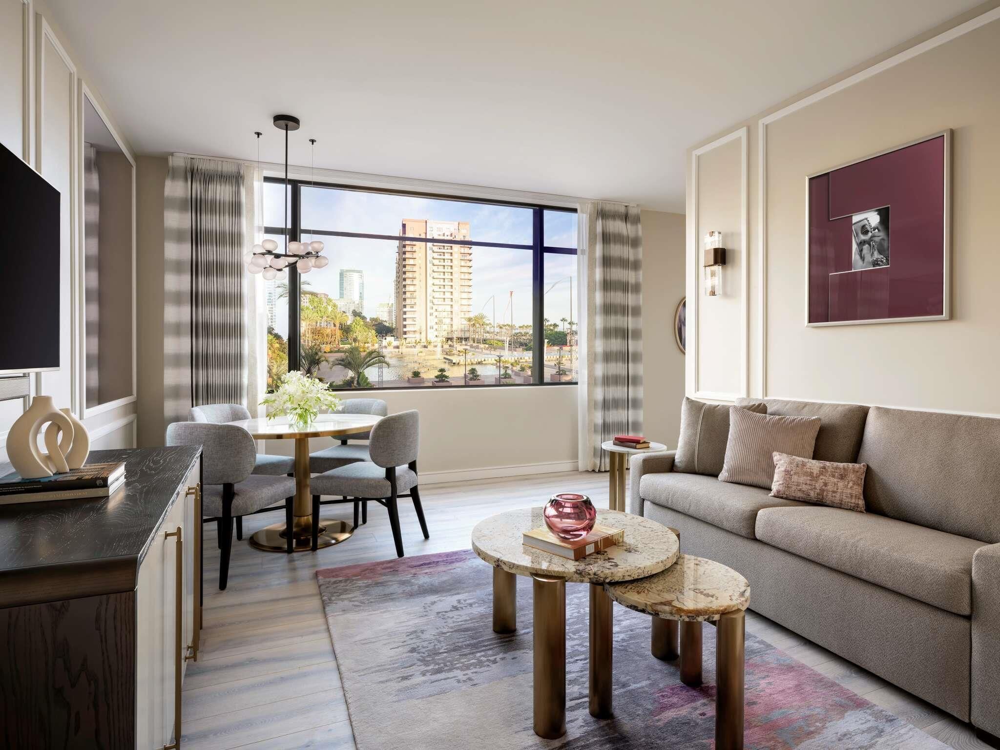 Una sala de estar moderna con un sofá, una mesa de comedor con sillas, una mesa de centro y un ventanal con vista a la ciudad.