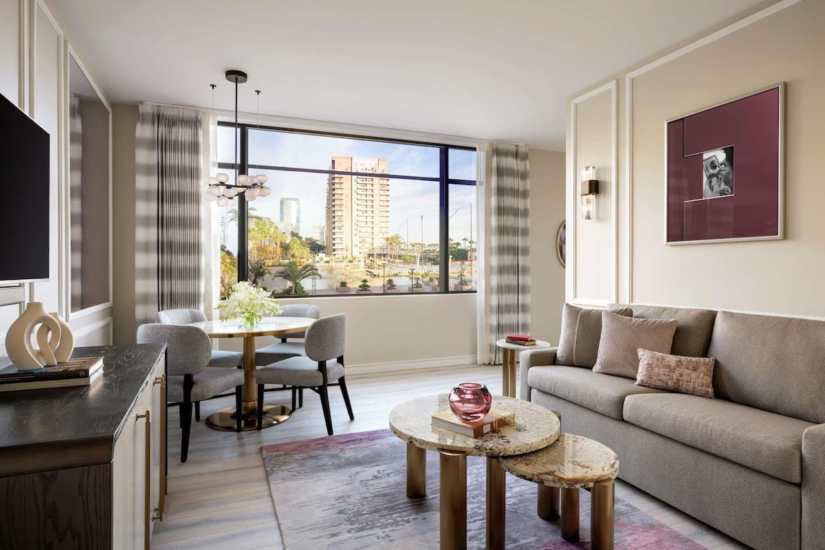 Una sala de estar moderna con un sofá, una mesa de comedor con sillas, una mesa de centro y un ventanal con vista a la ciudad.