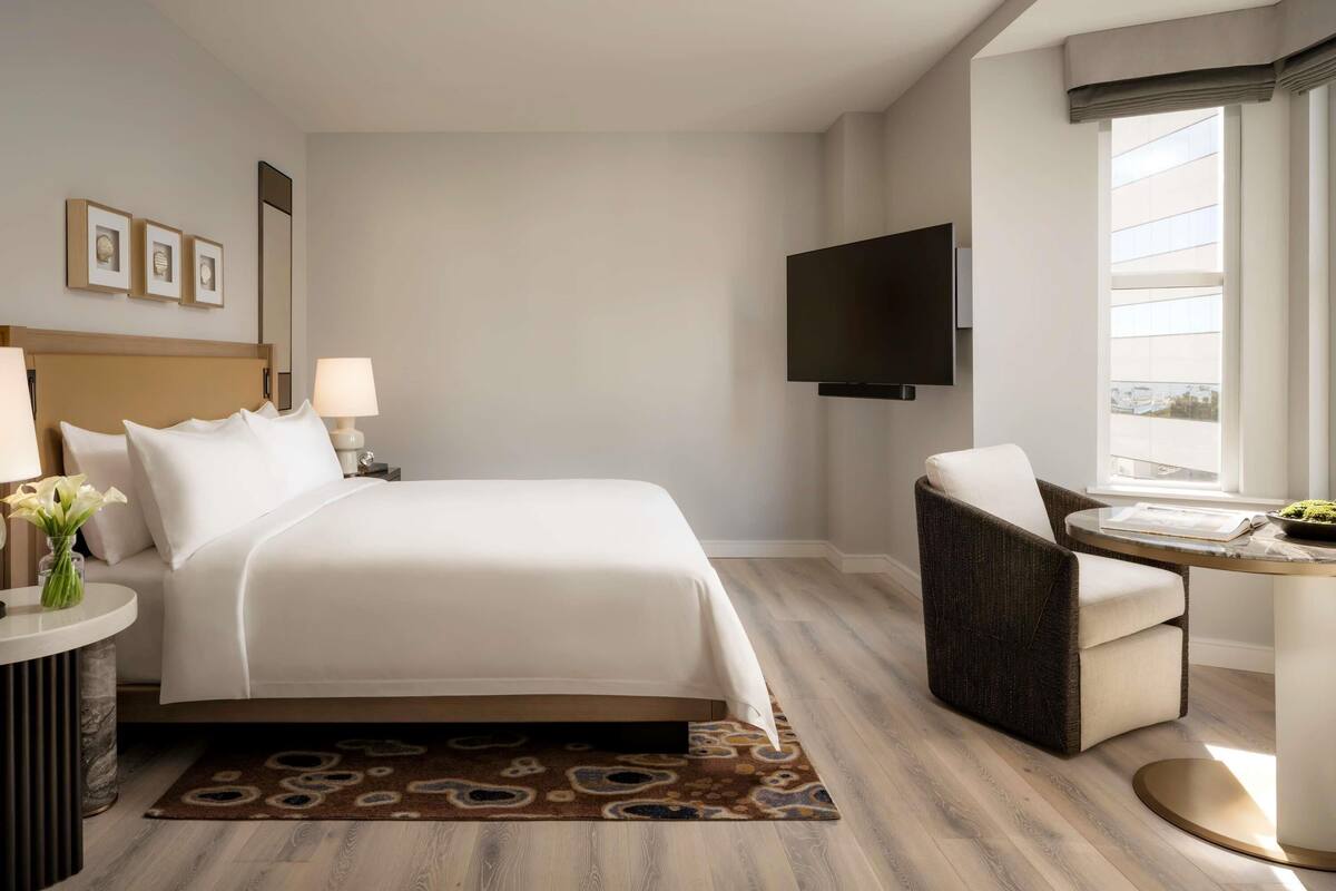 Een hotelkamer met een groot bed, een flatscreen televisie, een stoel en een tafeltje met een bloemenvaas.