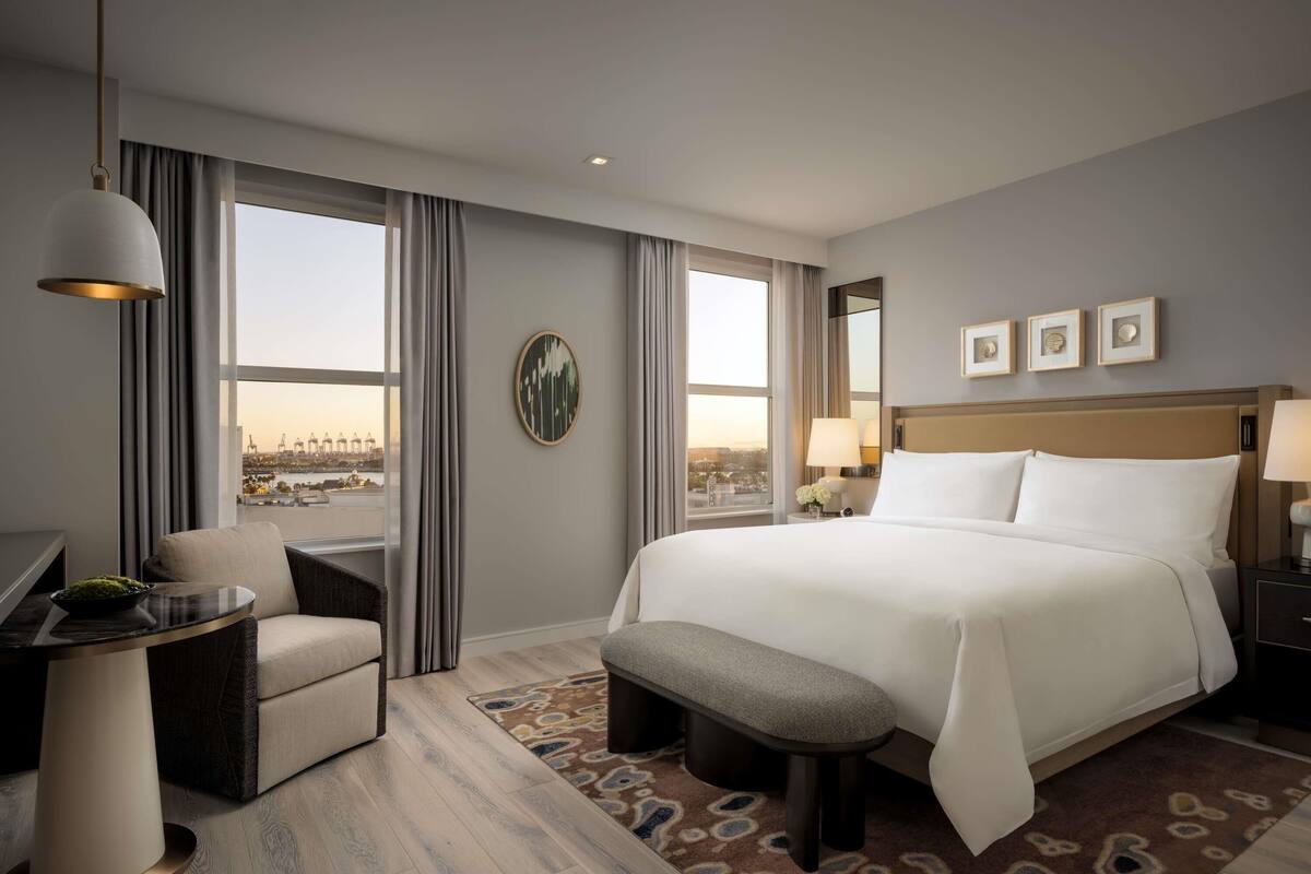Hotelkamer met een groot bed, een bureau, een stoel, een bankje, uitzicht op de stad en een groot raam.