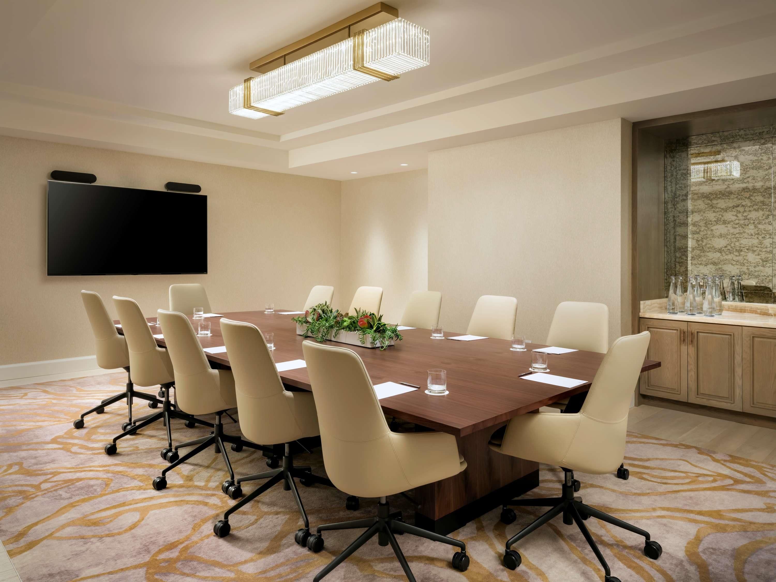 A conference room with a large table, chairs, a flat-screen TV, and a decorative plant centerpiece.