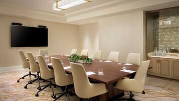 A conference room with a large table, chairs, a flat-screen TV, and a decorative plant centerpiece.