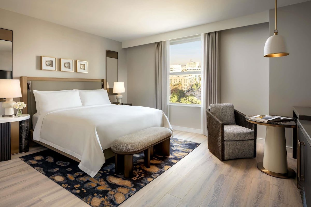 Habitación de hotel con una cama grande, una silla, un escritorio y vistas a la ciudad a través de la ventana.