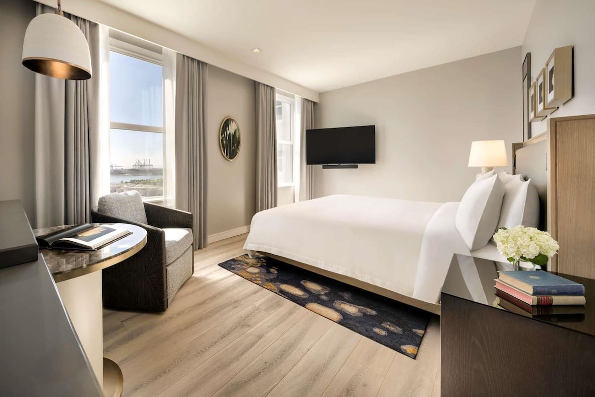 Habitación de hotel moderna con cama, escritorio, silla, televisor y vista a la ciudad.