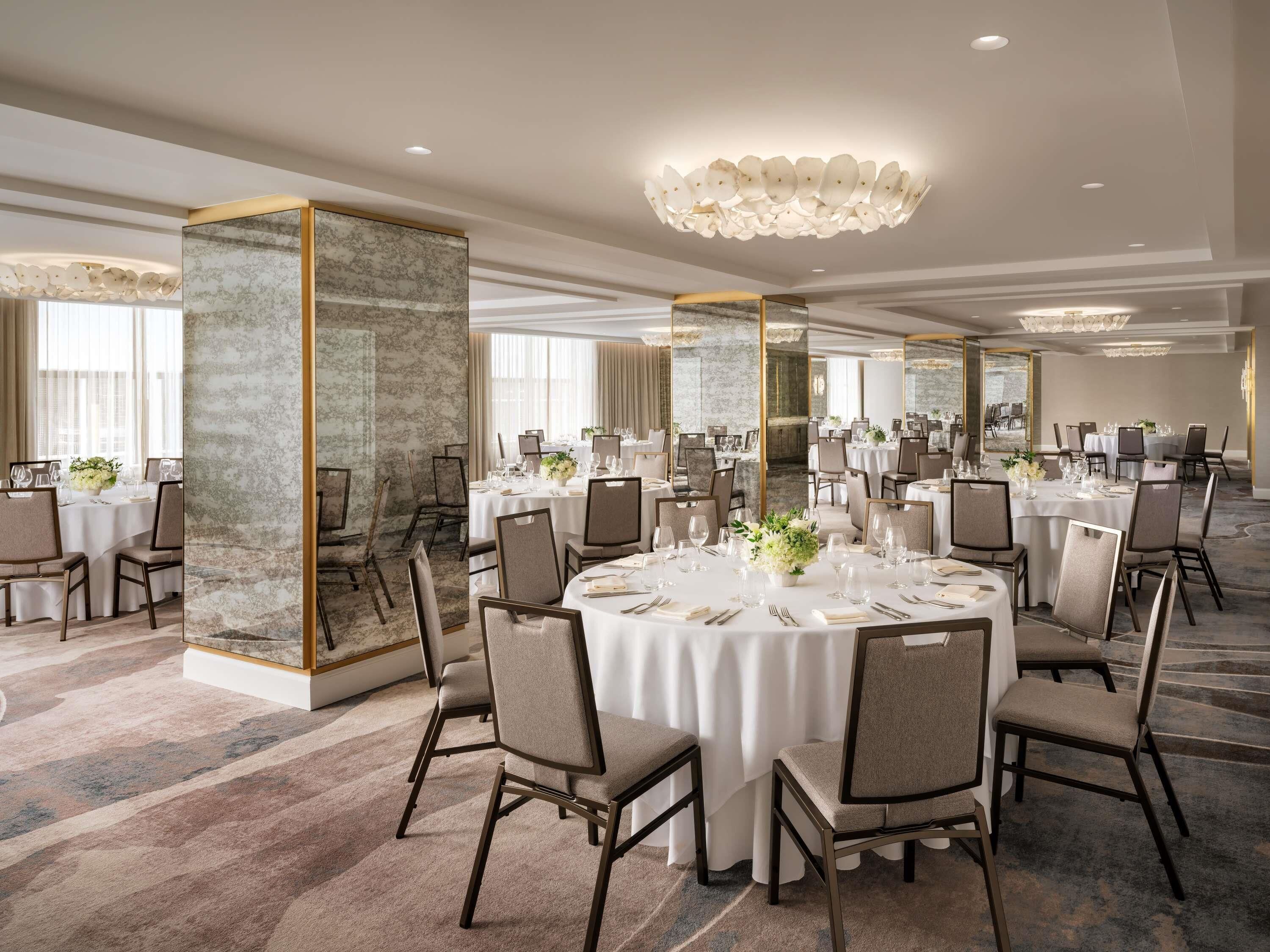 A spacious banquet hall with round tables, chairs, and a chandelier.
