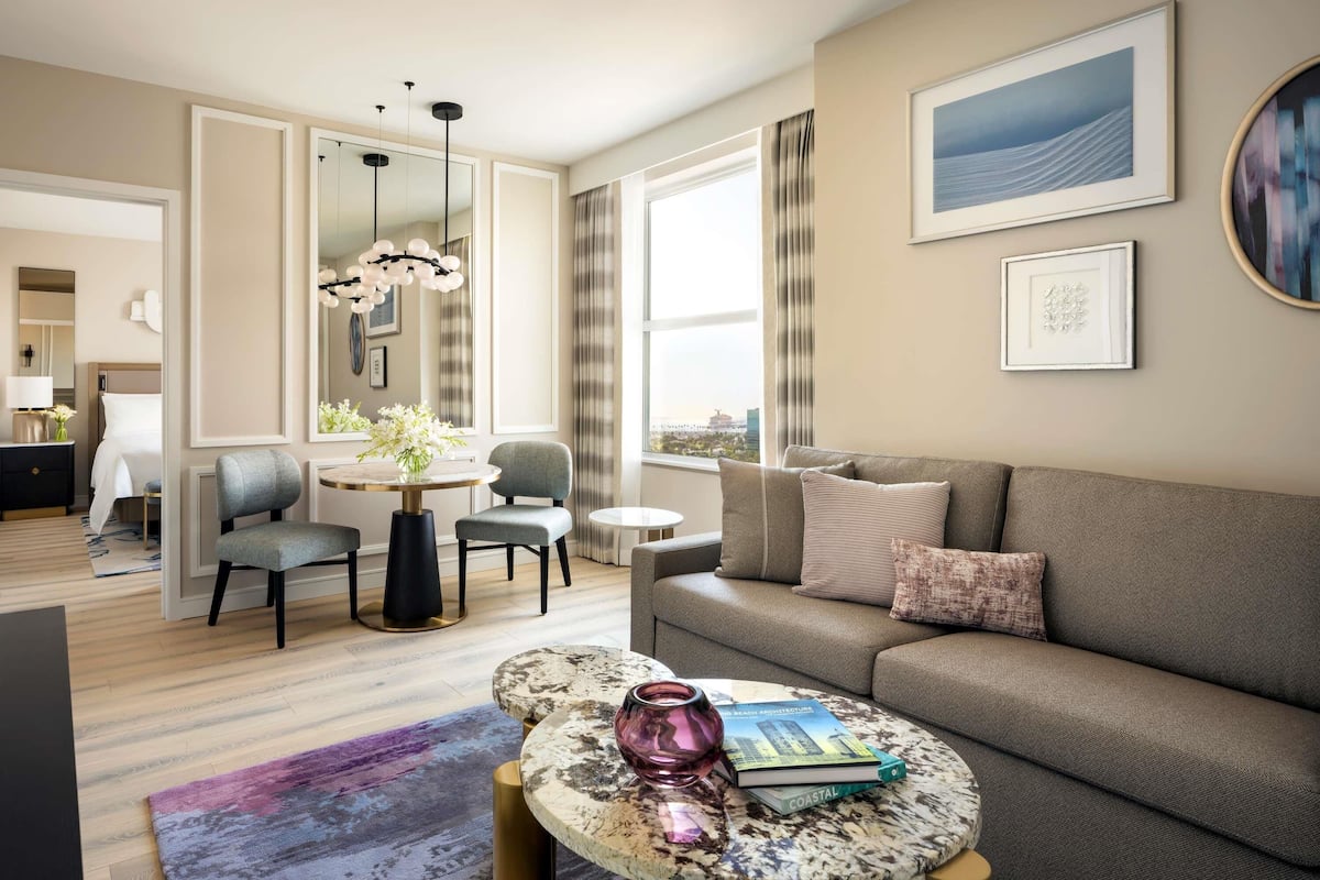 Een moderne woonkamer met een bank, een ronde salontafel, een eethoek met een kroonluchter en uitzicht op de stad.