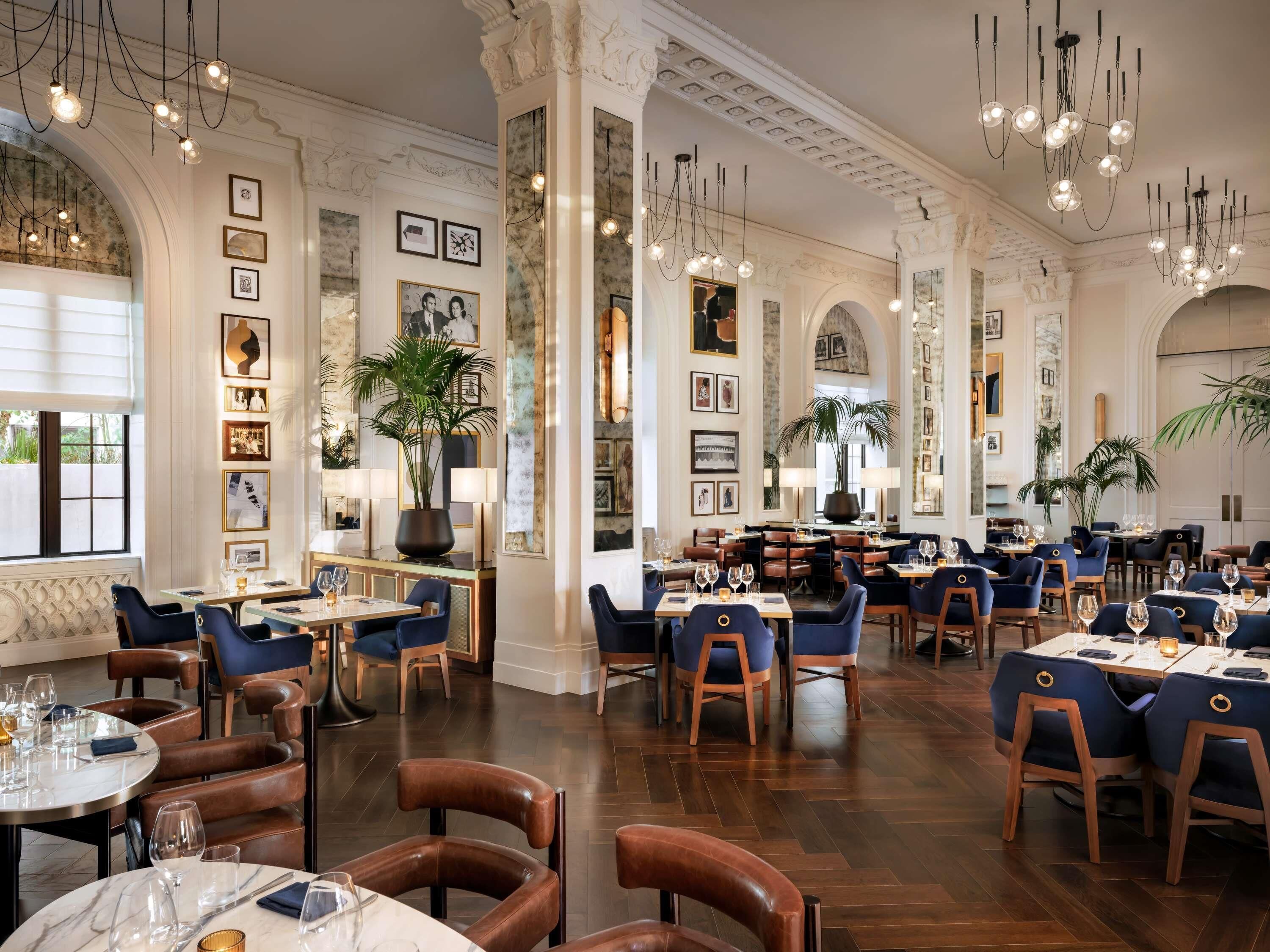Um restaurante espaçoso com tetos altos, lustres e decoração clássica.