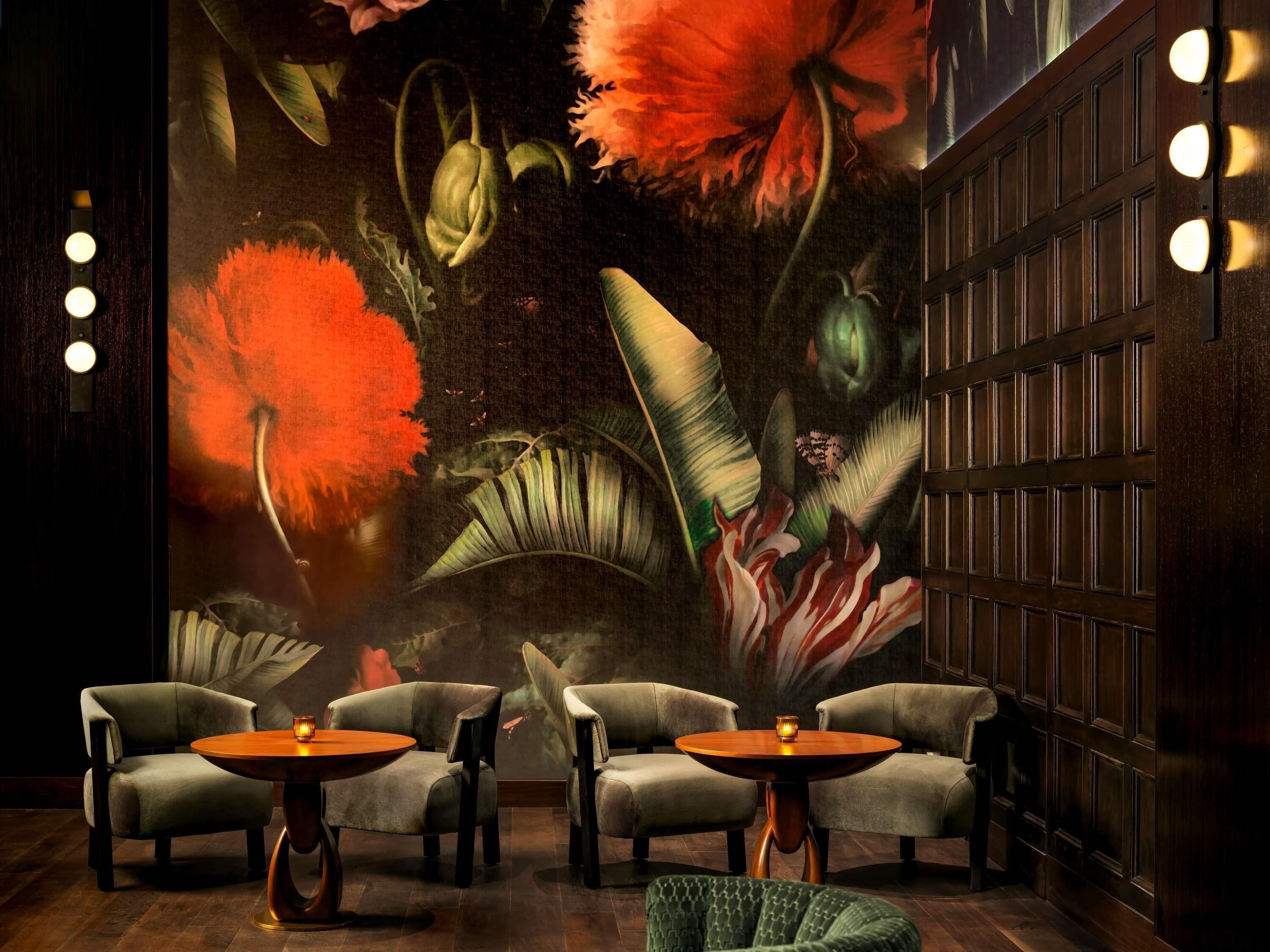 A room with a mural of tropical flowers, four armchairs, and a wooden table.