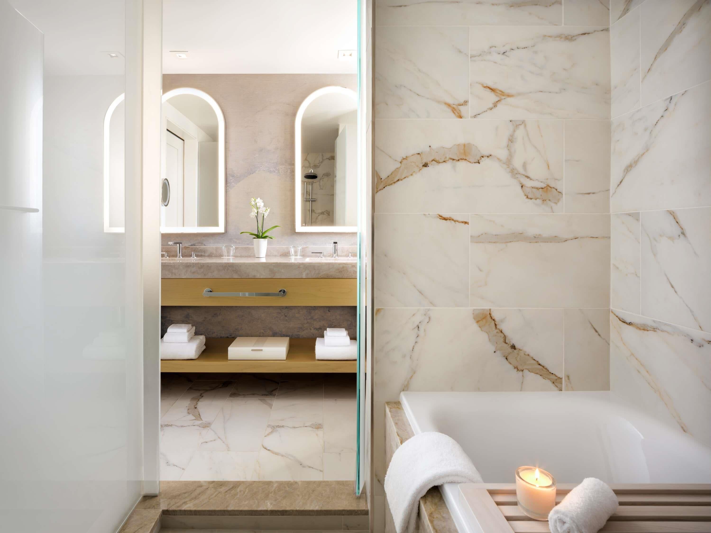 Une salle de bain moderne avec un sol en marbre, une baignoire, un meuble-lavabo avec un miroir et un porte-serviettes.