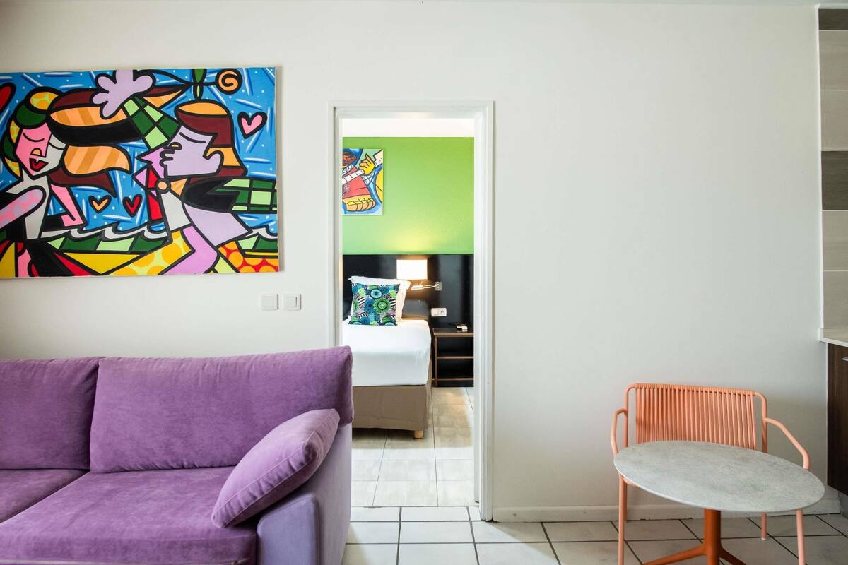 A room with a purple sofa, a small round table, and a colorful abstract painting on the wall.