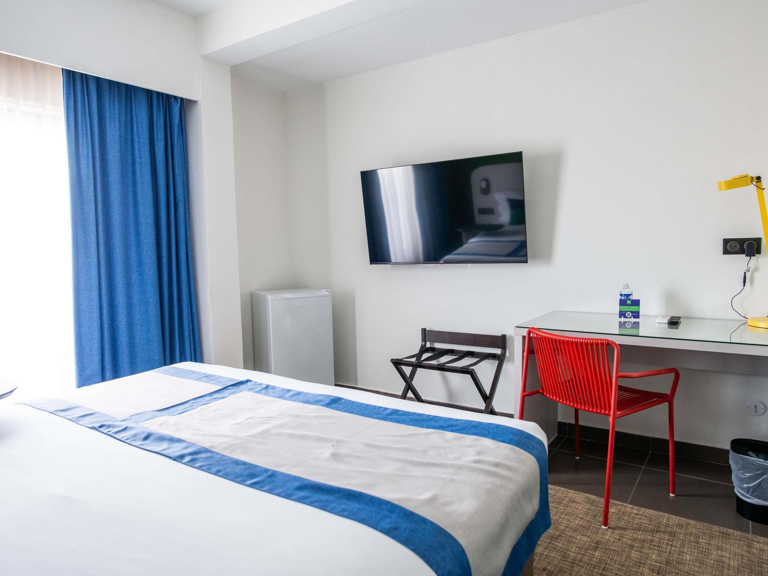 A hotel room with a bed, a desk, a chair, a TV, and a trash bin.