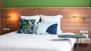 Una habitación de hotel con cabecera de madera, cama con ropa blanca y dos almohadas decorativas.