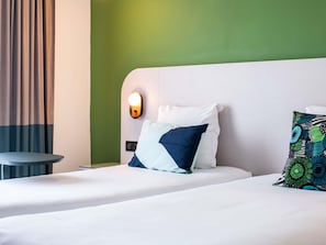 A hotel room with a bed, a nightstand, a wall-mounted light, and a green accent wall. - Ibis Styles Cayenne Centre Amazonia (Ouverture Juin 2024) (Cayenne)